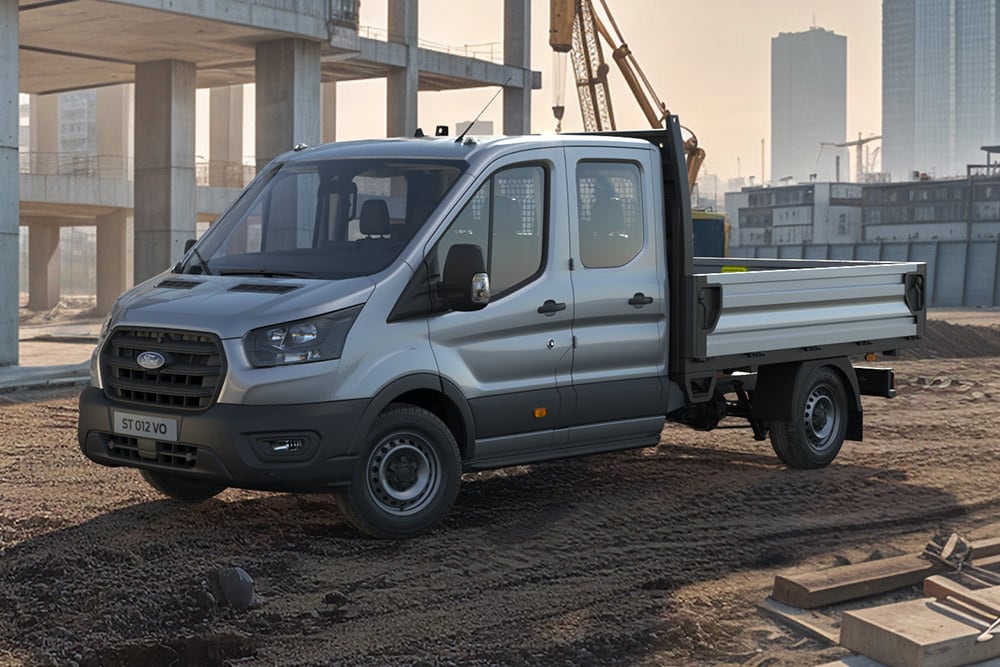 Ένα ασημί Ford Transit ανατρεπόμενο με διπλή καμπίνα στέκεται σε εργοτάξιο, με γερανό στο βάθος.