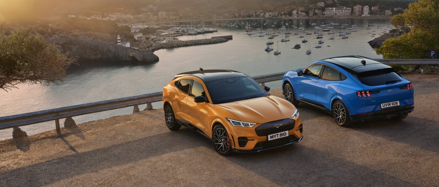 An orange and a blue Mustang Mach-E GT parked near the sea