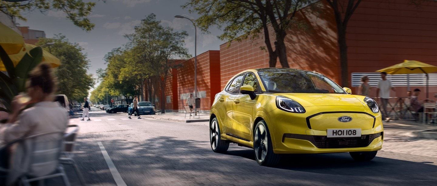 Μπροστινή άποψη ενός κίτρινου ηλεκτρικού Ford Puma Gen-E® που κινείται σε δρόμο της πόλης.