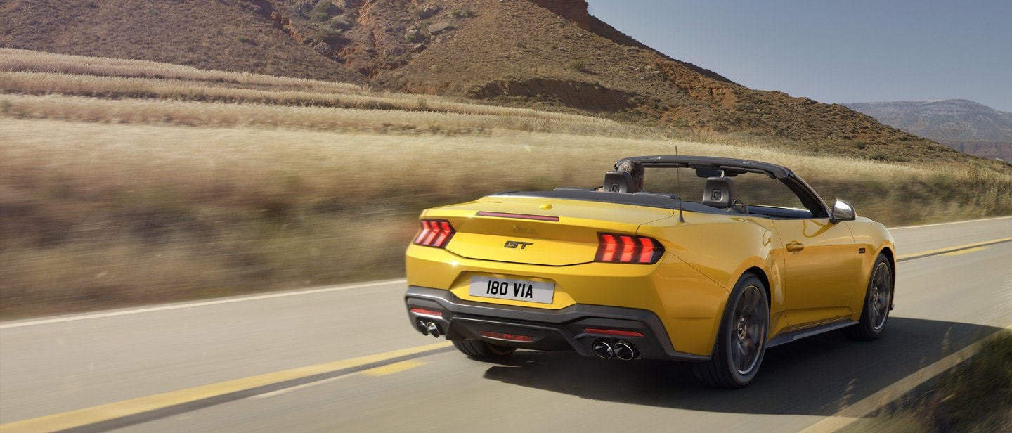 Yellow Ford Mustang riding a road rear view