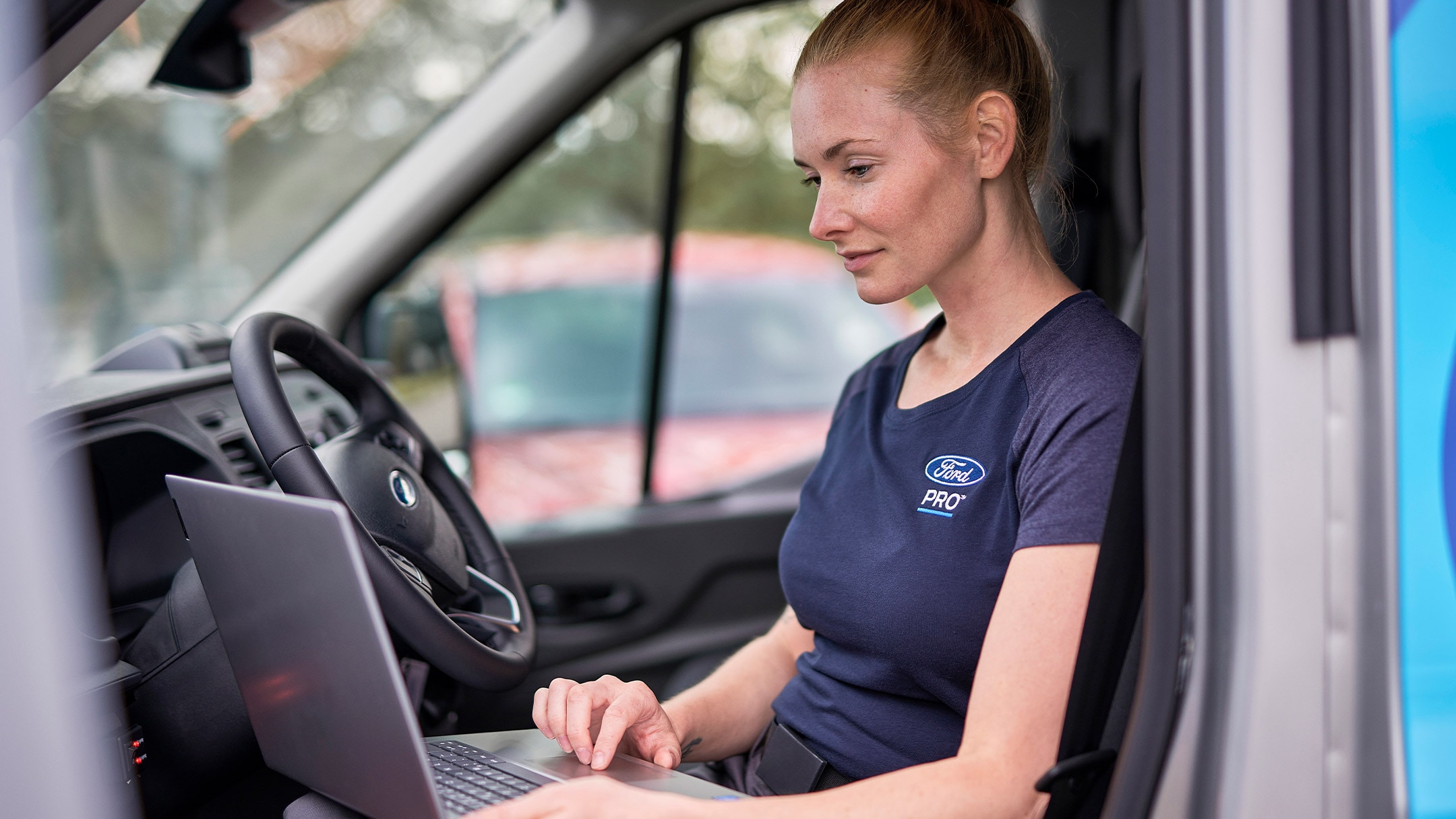 Ένας ειδικός Ford Pro κάθεται σε ένα αυτοκίνητο ελέγχοντας έναν φορητό υπολογιστή κατά τη διάρκεια ενός σέρβις οχήματος Ford.