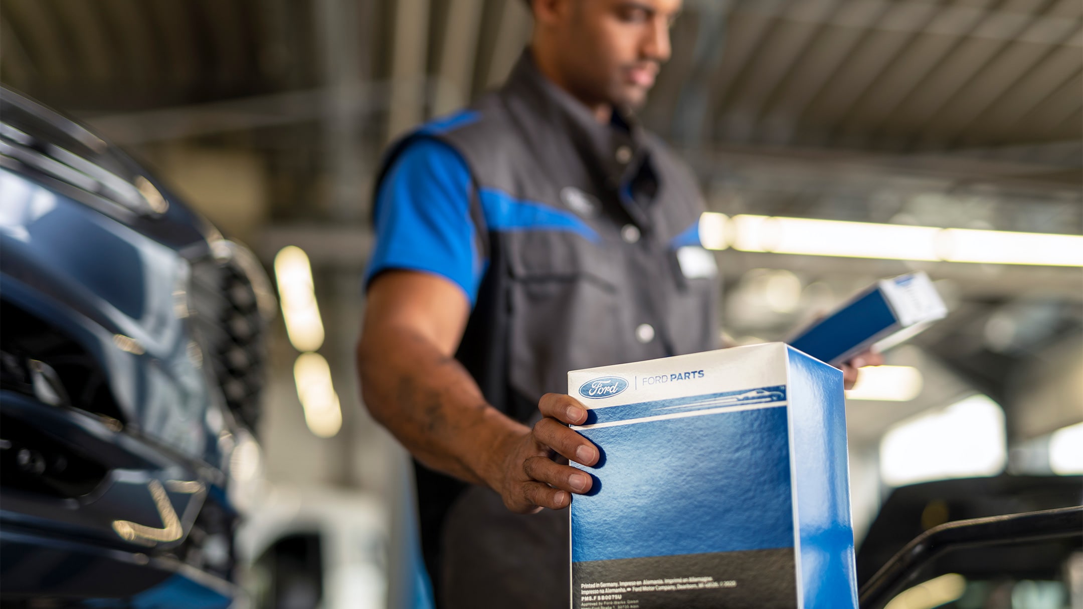Ένας μηχανικός σε ένα κατάστημα Ford service κρατά ένα γνήσιο ανταλλακτικό αυτοκινήτου Ford συσκευασμένο σε ένα επώνυμο κουτί.